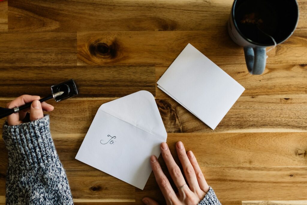 A hand writing a letter beside a cup of coffee
