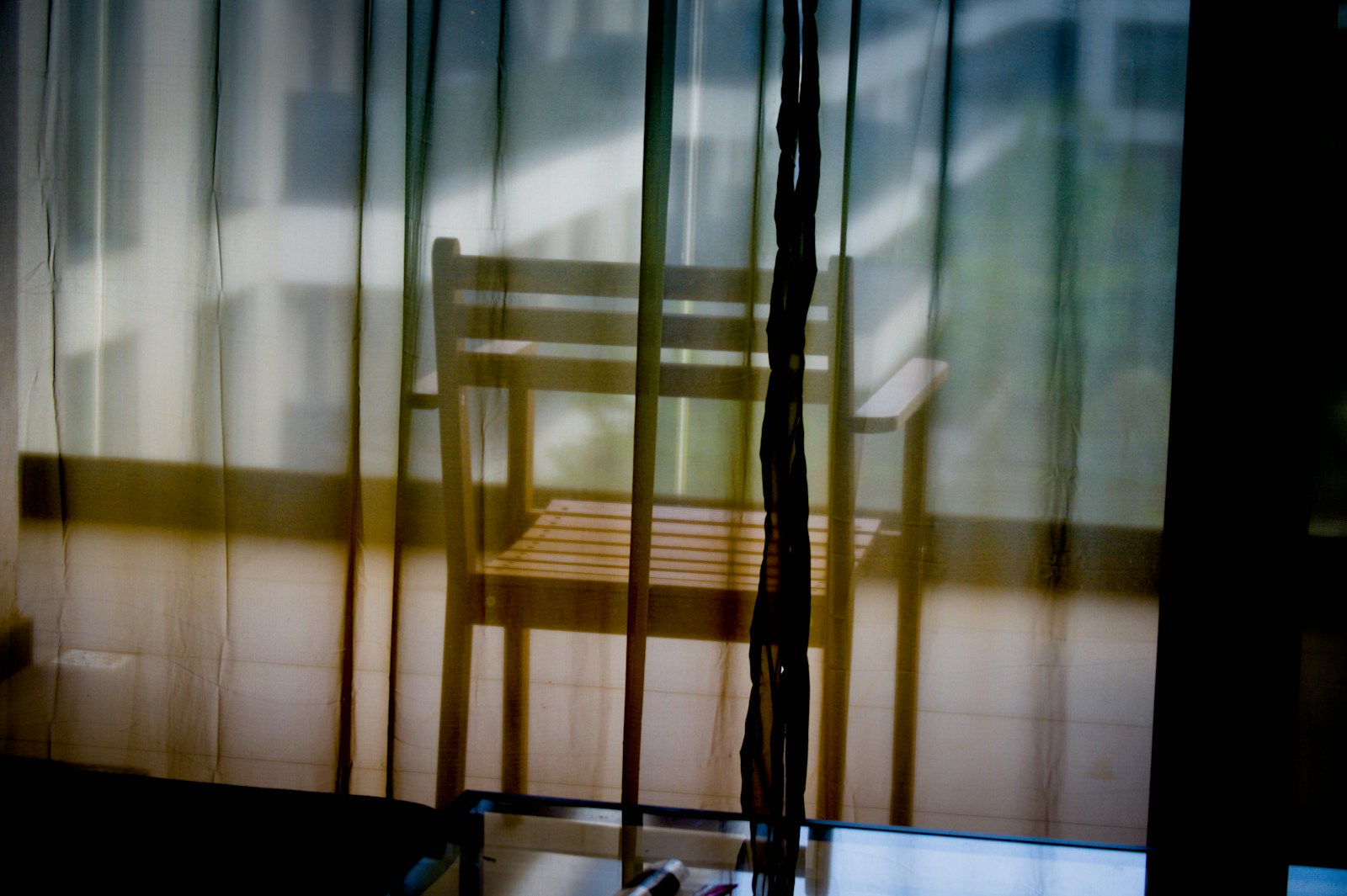 An empty wooden chair seen through sheer curtains